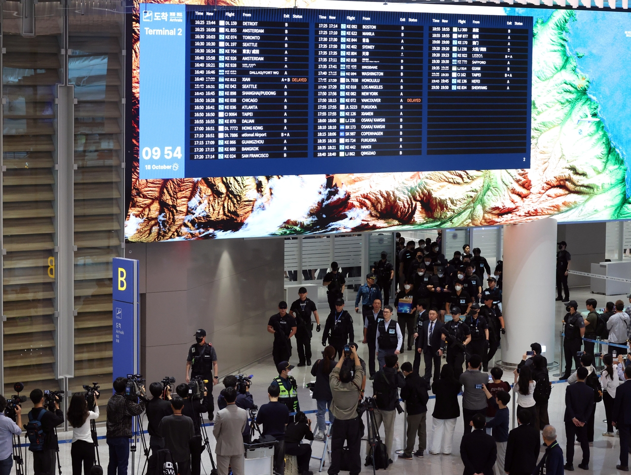 South Korean police escort 64 nationals repatriated from Cambodia at Incheon Airport on Oct. 18. The group is accused of participating in cross-border scam networks run out of compounds where many were reportedly held against their will and forced to target fellow Koreans through voice phishing and fake investment scams. (Joint Press Corps)